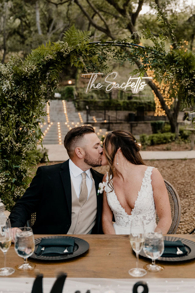 bride and groom kissing with their names behind them on their wedding day at their sweetheart table