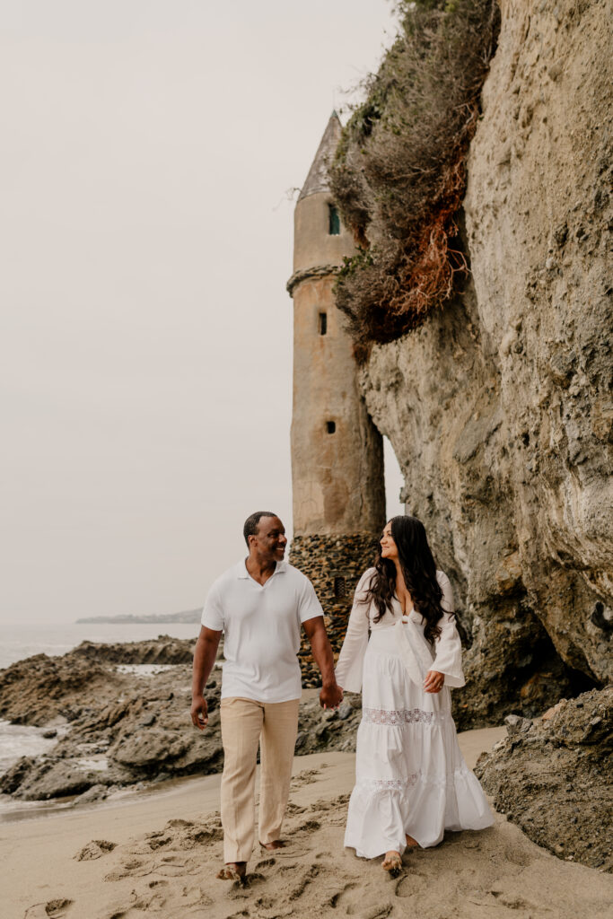 Victoria Beach Engagement session at pirates tower. a couple holding hands smiling at each other with the castle in the background